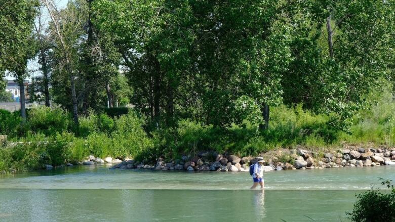 A person is pictured walking through a body of water on a hot day.