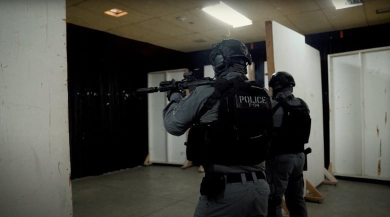 Two officers in tactical gear holdings guns.