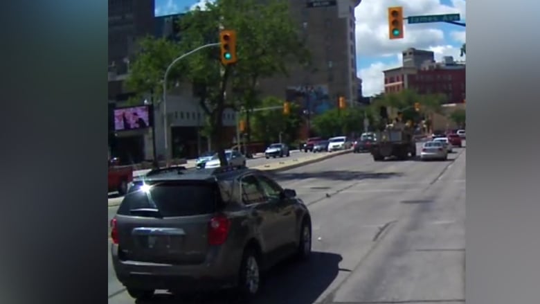 A surveillance still shows a grey SUV driving down a busy street.