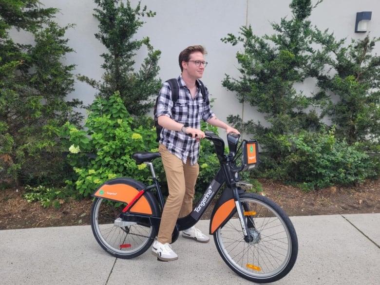 Man stands astride an orange and black bicycle