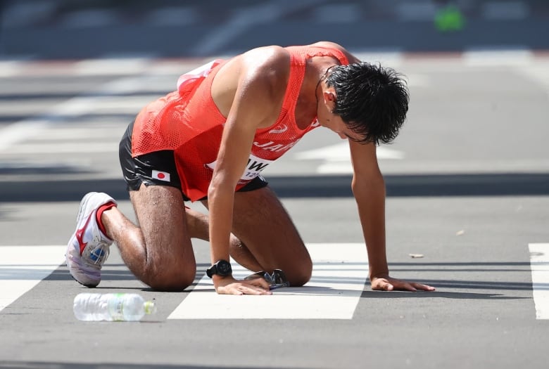 Masatora Kawano of Japan falls on his knees, covered in sweat, after finishing the Men's 50km race walk at the Tokyo Olympics, August 6, 2021.