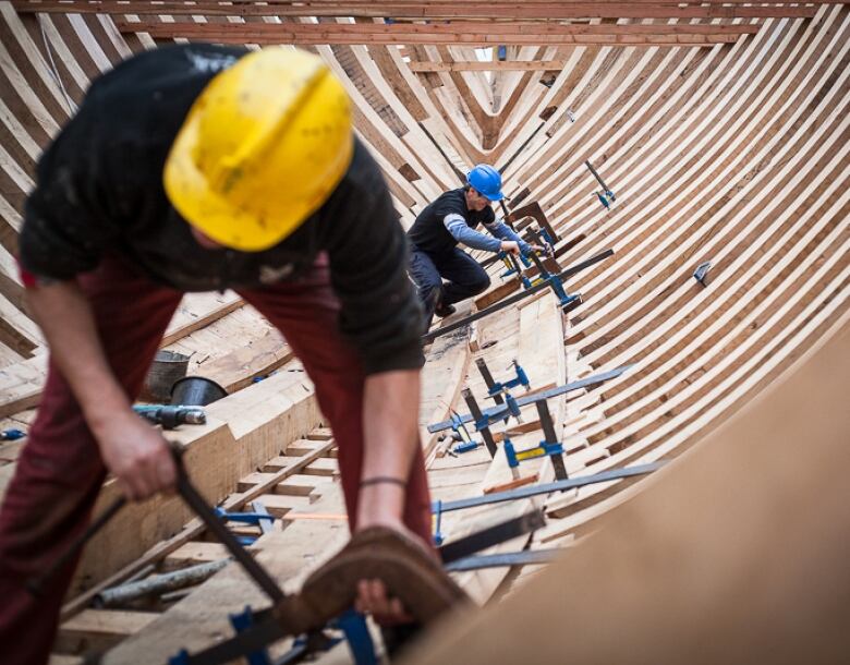 Two workers adjust clamps as they work on a large ship