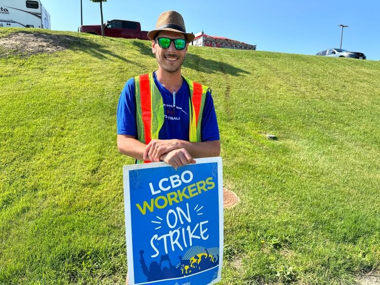 A man wearing an orange safety vest with a blue sign that says, 'LCBO workers on strike.'