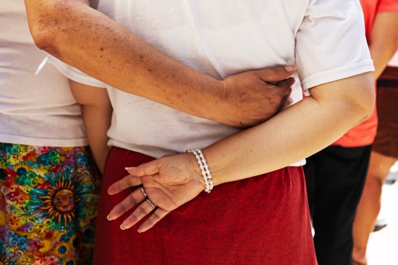 A person wearing a ribbon skirt puts their hand around the back of someone else wearing a ribbon skirt.