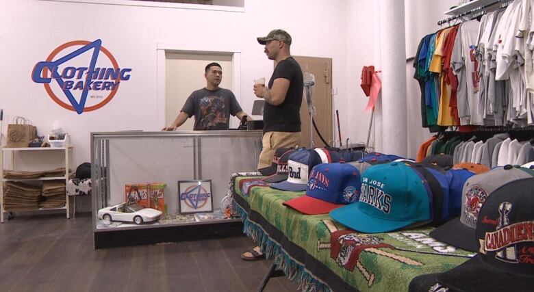 A man at a store with some vintage clothes talking with a customer.