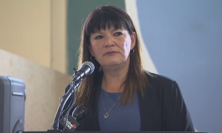 A woman with long brown hair speaks at a podium