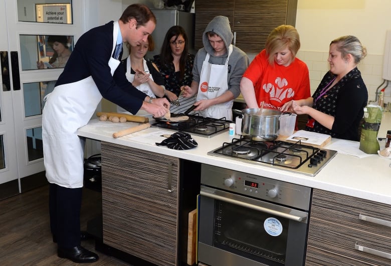 Several people stand and work around a cooktop.