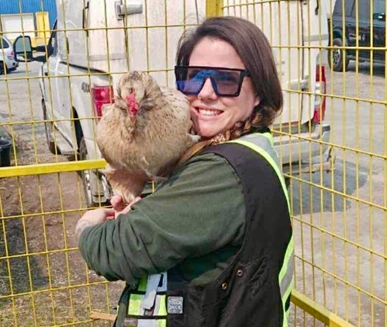 A woman in sunglasses holds a live chicken.