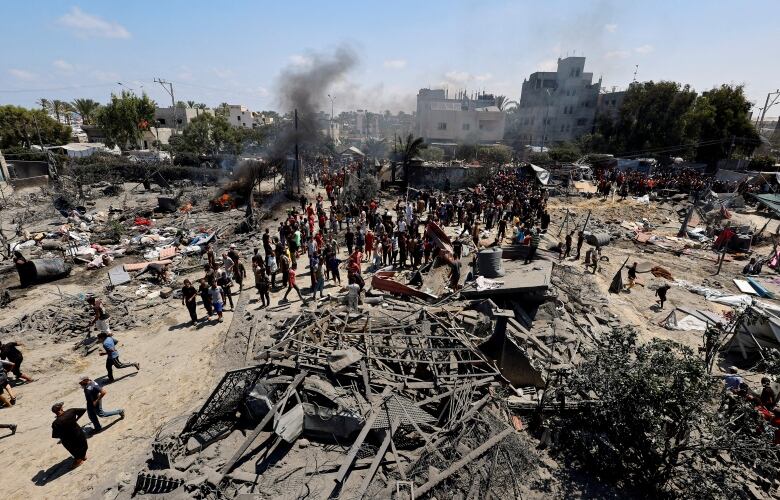 An overhead view shows people gathering around the smoldering debris of destroyed buildings.