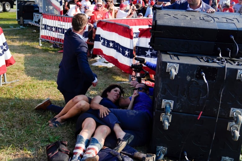 People take cover by lying on the ground next to a stage.