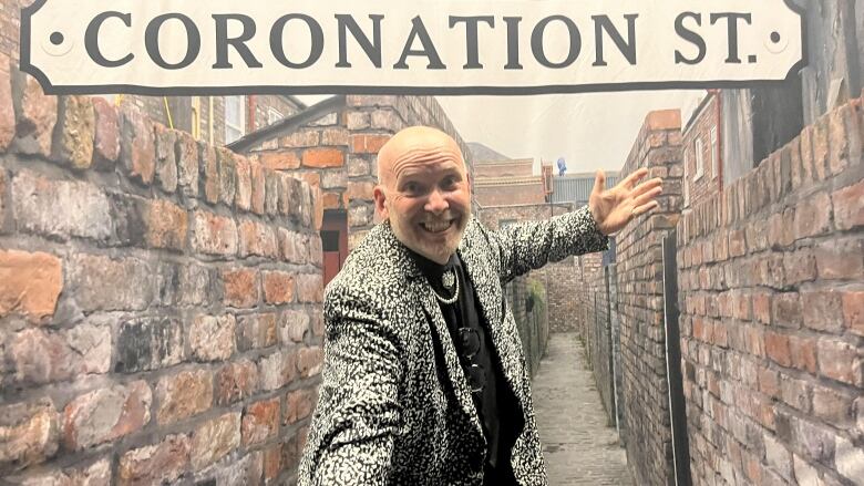 A man smiles in front of a Coronation Street screen. 