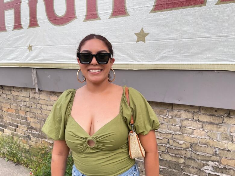 A woman wearing a green top, black sunglasses and gold hoops smiles.