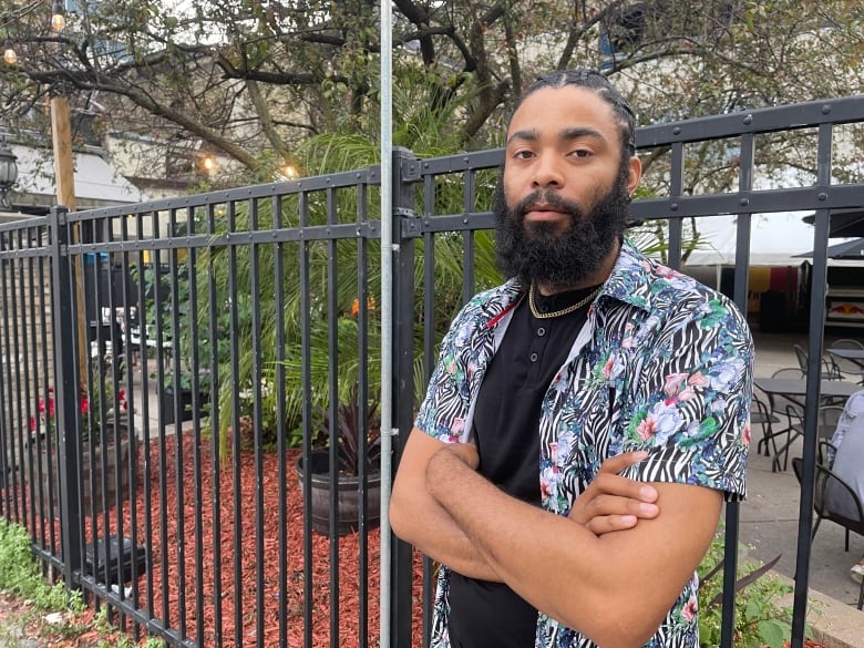 A man wearing an animal print shirt and a gold chain crosses his arms.