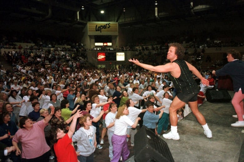 A person onstage gestures to an audience that mimics the gesture.