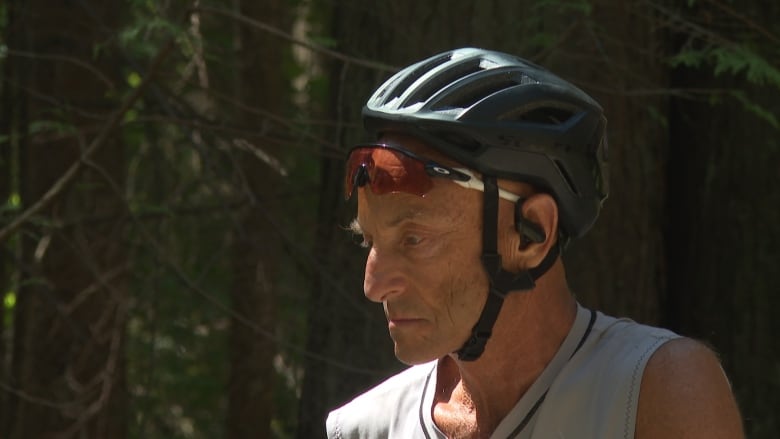 A cyclist in forested part of a park has a helmet on and has balanced his shades on his forehead.