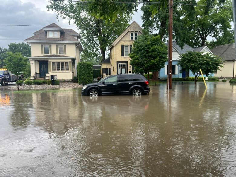 Black SUV parked on a flooded road in a residential neighbourhood. 