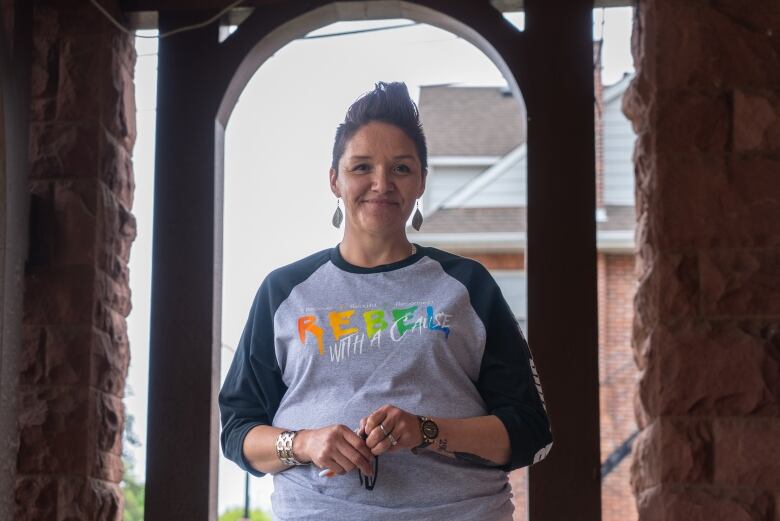 A person is seen standing on a front porch between an archway, smiling. 