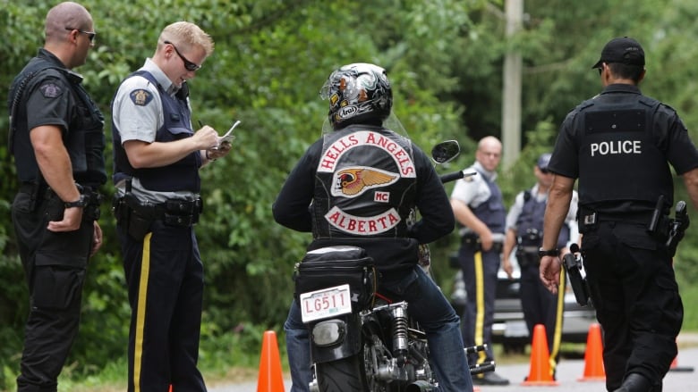 A motorcycle stops on the side of a street to talk to a man in a uniform. 