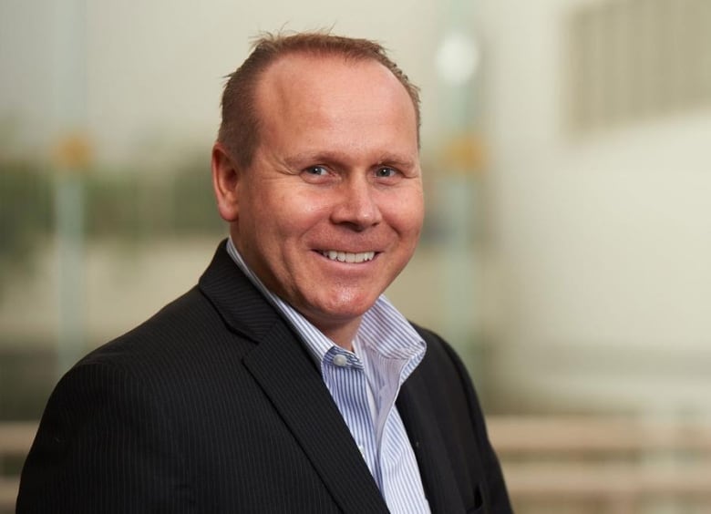 A man wearing a black suit and a blue and white shirt underneath it.