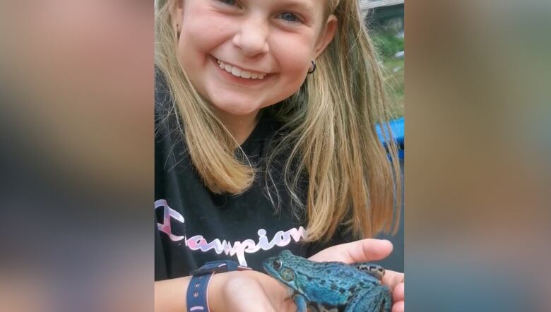 A white girl with blonde hair smiling, she is holding a rare blue frog in her hands.