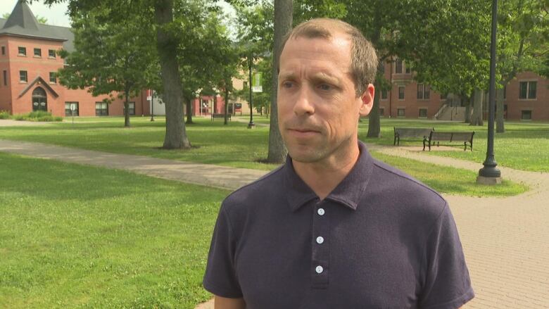 Man in navy blue golf shirt standing on a university campus.