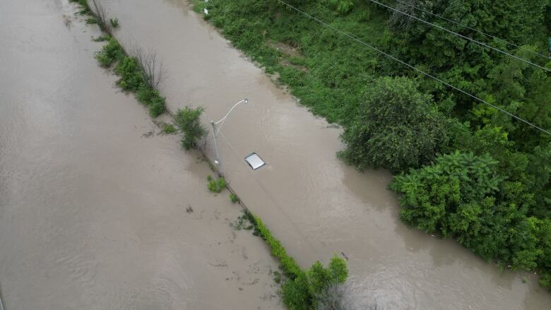 A drone image shows the top of a vehicle barely visible above water on the flooded DVP. 