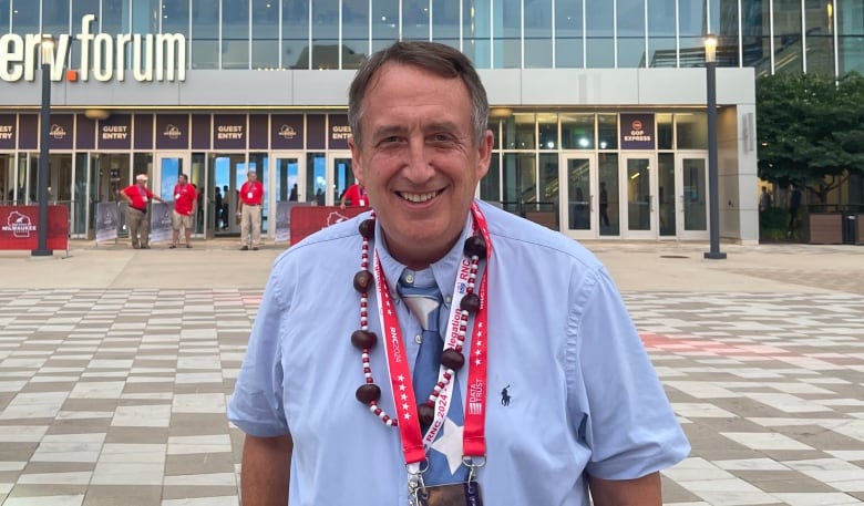 A man wearing a blue shirt and several lanyards around his neck smiles.