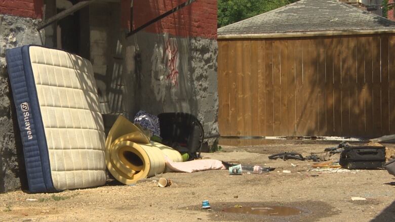 A pile of clothes and furniture lays on the ground near a dumpster. 