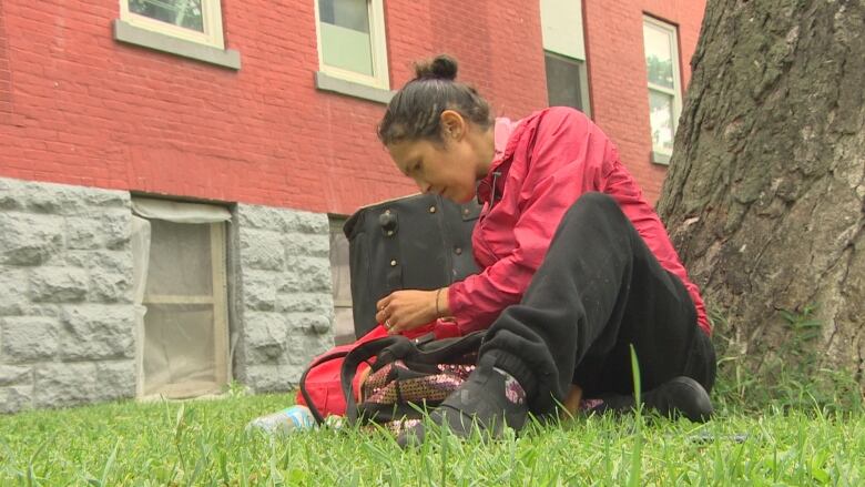 A woman sits on the grass outside an apartment with several suitcases. 