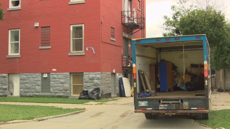 A moving truck can be seen in front of a building with furniture up against the brick. 