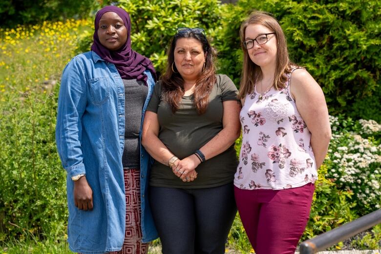 three women stand in from of trees and flowers