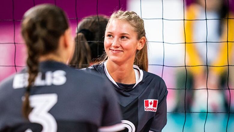 A woman sits in front of a volleyball net wearing a Team Canada jersey.