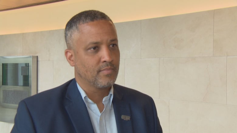 A man with a short beard and hair wearing a suit looks slightly off camera