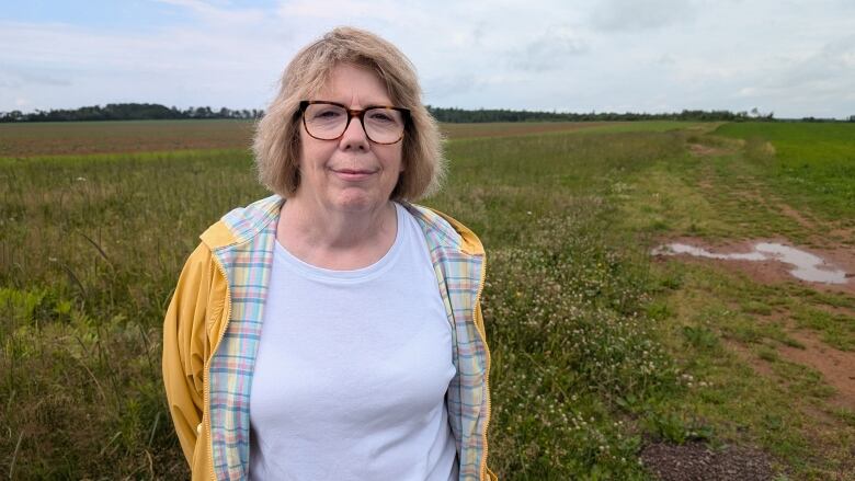 A woman in a yellow jacket stands with a potato field in the background 