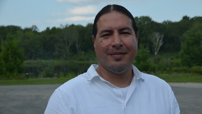 A man in a white shirt with trees behind him 