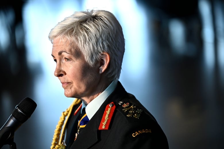 A woman with white hair and a military uniform speaks into a microphone.