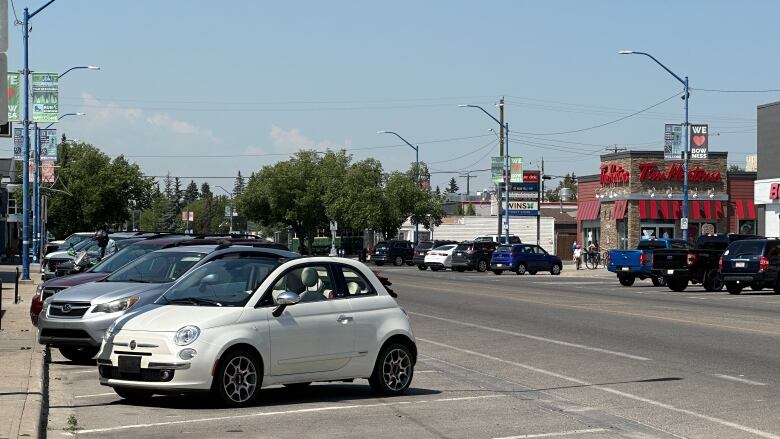 Vehicles parked on a road with stores and trees.