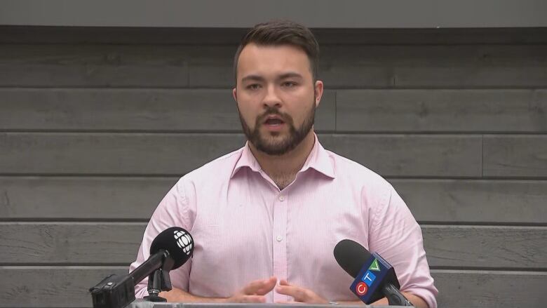 A man in a pink shirt stands at a podium.