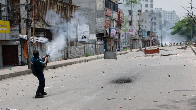 A police officer fires tear gas on a street with debris.