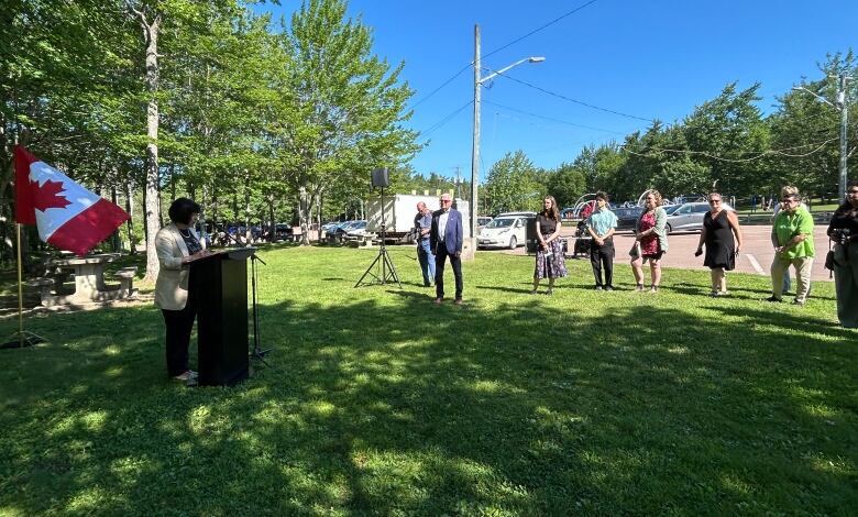 An announcement taking place in a park. A speaker on podium and people standing in a park.