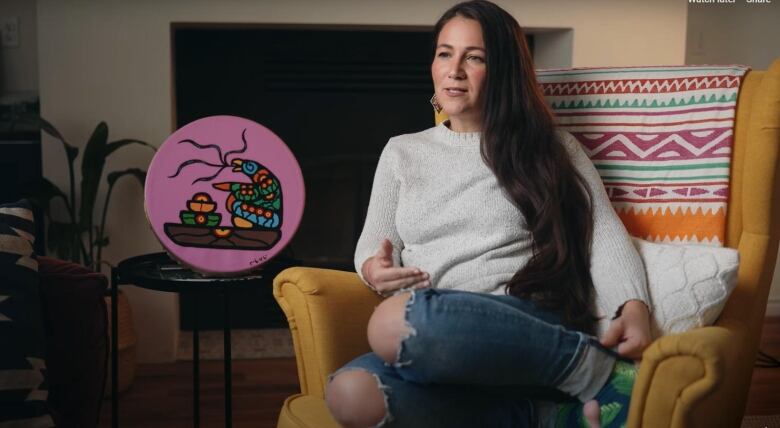 Woman with long dark hair curled up in an armchair