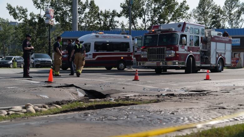 a hole in the road. caution tape is around the hole and firefighters are standing near it.