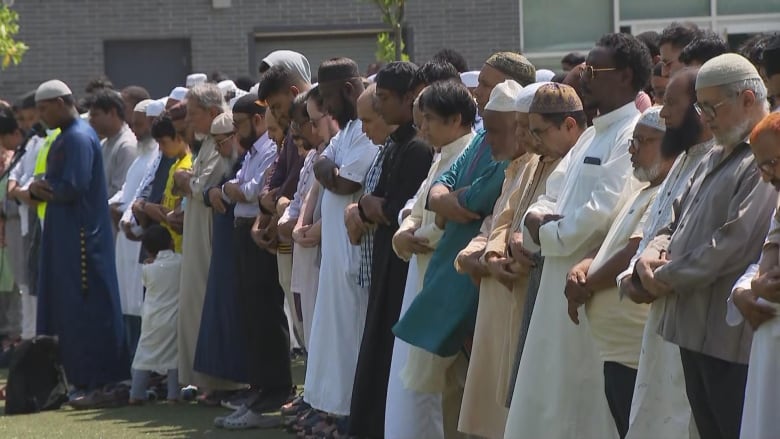 People stand in a line with their heads bowed and arms crossed.