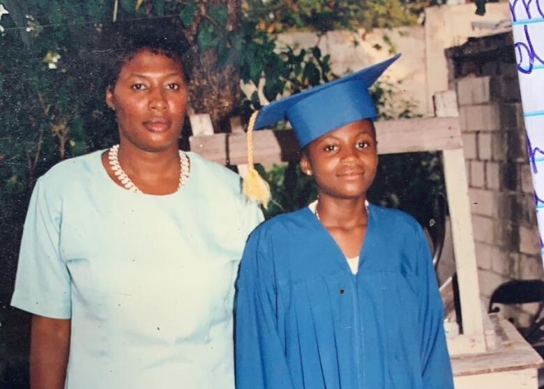 A young girl in a blue graduation cap and gown with her mother. 