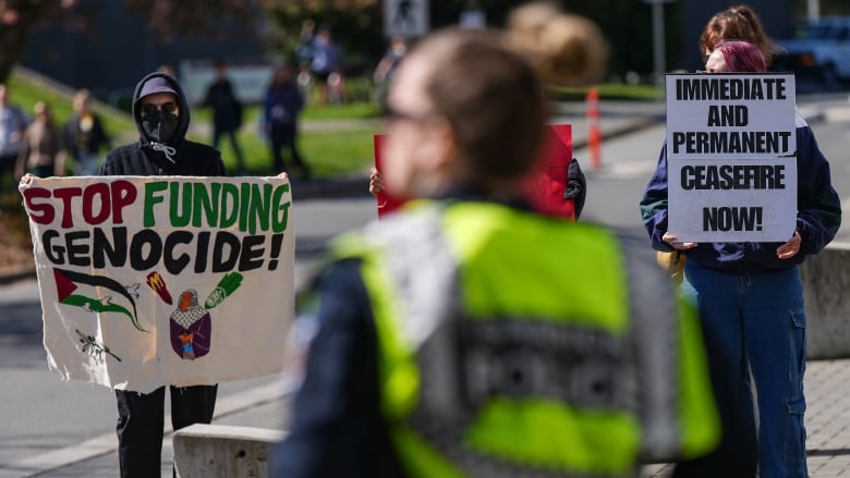 Two protesters hold up signs reading 'Stop funding genocide' and 'Immediate and permanent ceasefire now!'