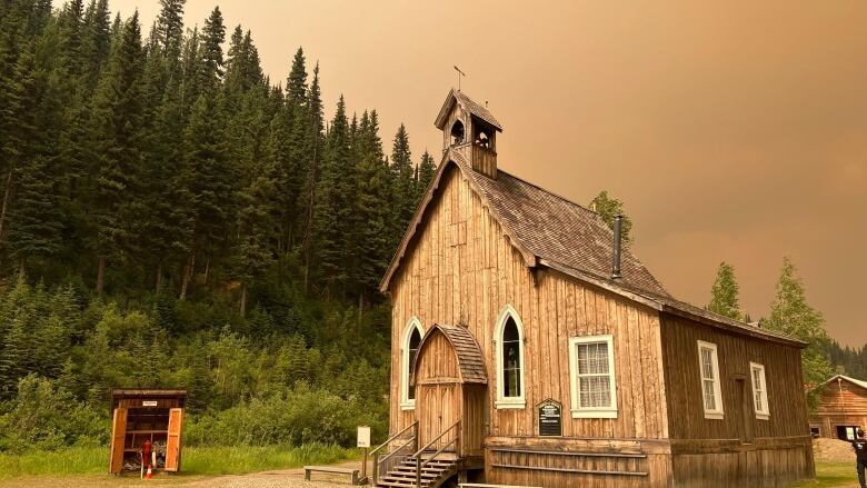 A rustic church with forest behind and wildfire smoke casting a pall over the town. 