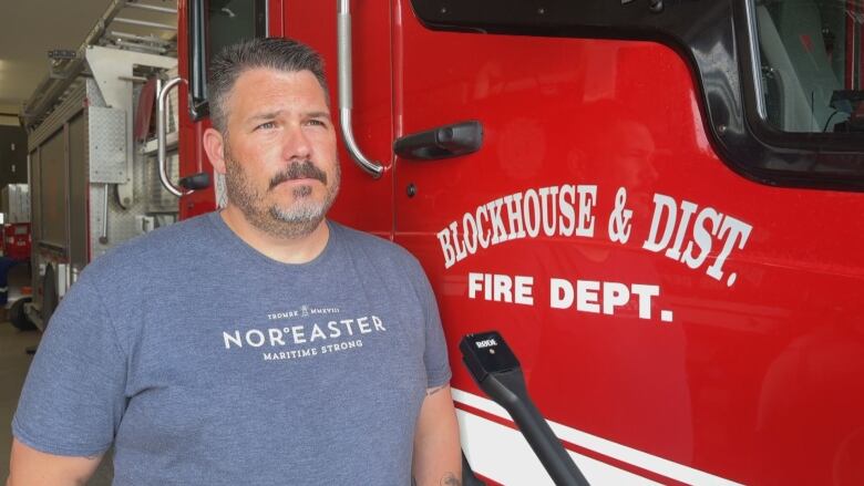 A man wearing a T-shirt stands next to a fire truck.