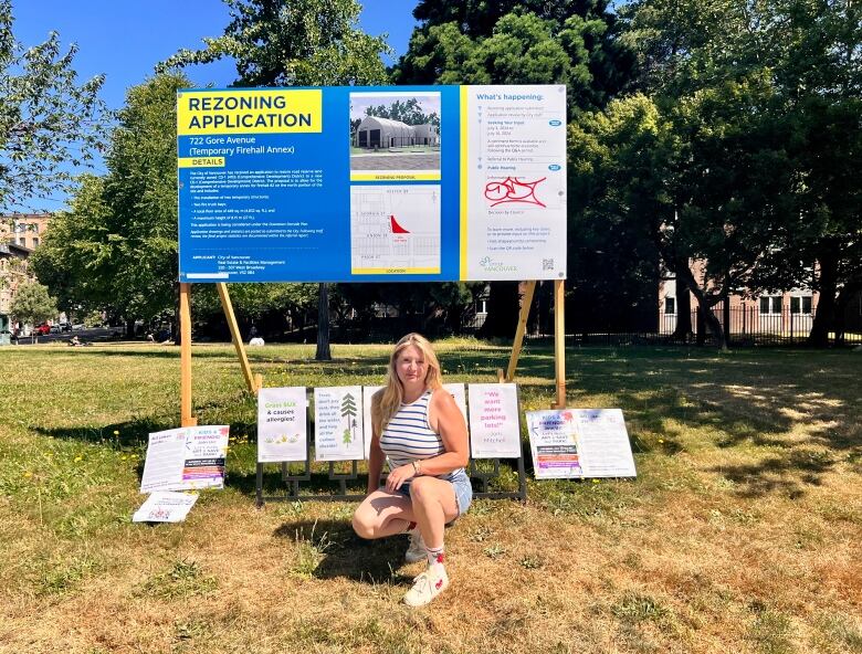 A woman stands in front of several city rezoning signs. 