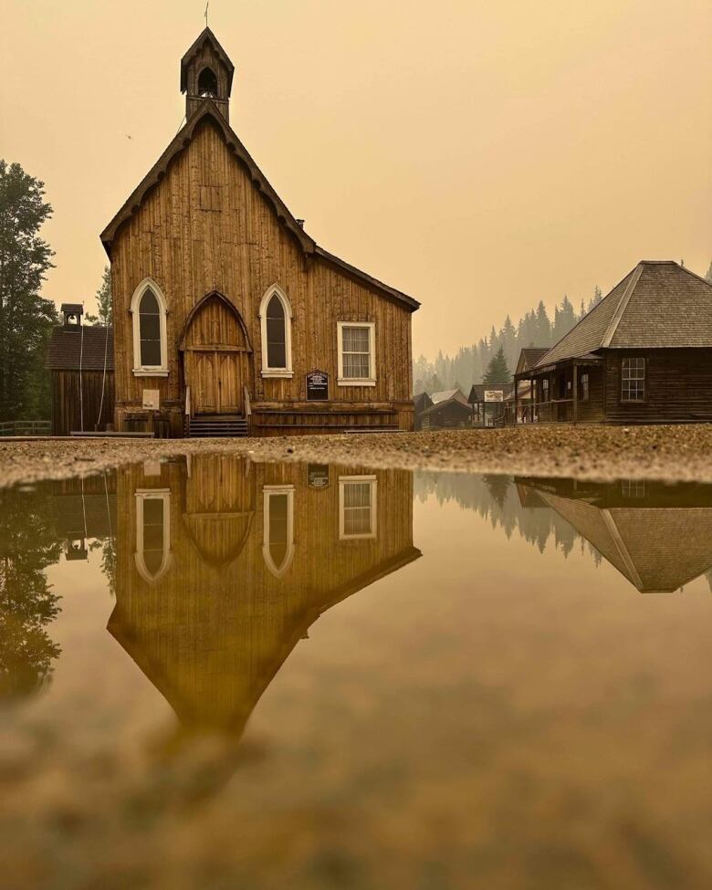 A structure in Barkerville and its reflection in a pool of water, under a smoky sky