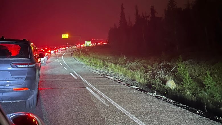 A long lineup of cars on a highway with red sky in the background.